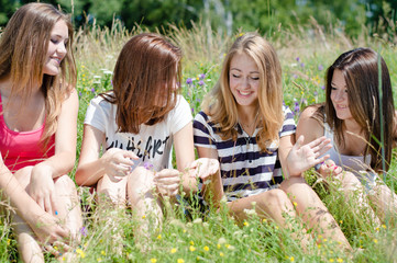 Four happy teen girls sitting on green lawn and sharing secrets