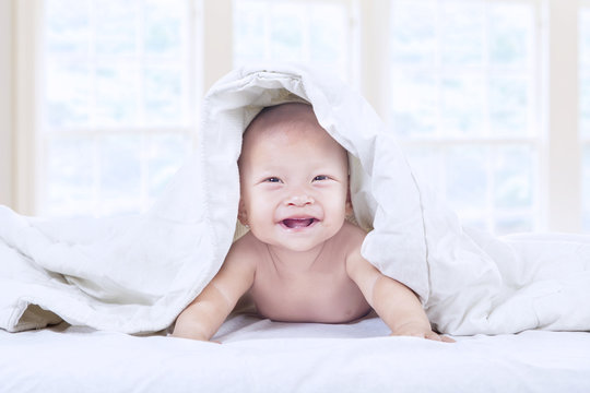 Cute baby laughing under blanket at home