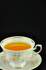 porcelain tea cup full of tea and green teapot on a black backgr