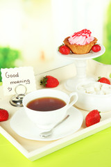 Cup of tea with cakes on wooden tray on table in room