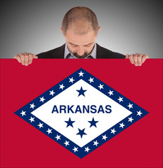 Smiling businessman holding a big card, flag of Arkansas
