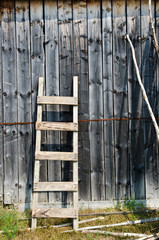 Old wood ladder leaning over a grey wooden wall. - 55626995