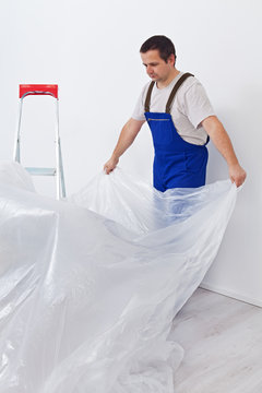 Worker laying down thin protective foil before painting