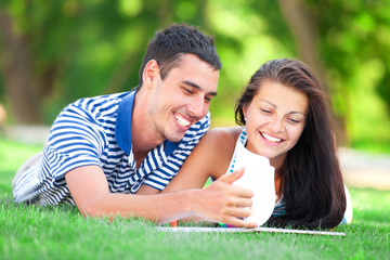 Young students sitting on green grass with note book.