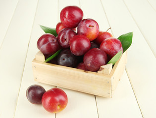 Ripe plums in wooden box on wooden table close-up