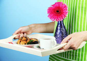 Woman in green apron holding wooden tray with breakfast,