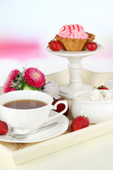Cup of tea with cakes on wooden tray on table in room