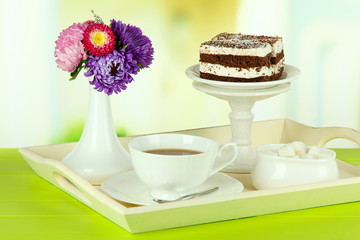 Cup of tea with cakes on wooden tray on table in room