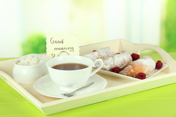 Cup of tea with cakes on wooden tray on table in room