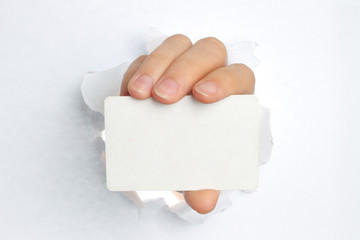 Hand holds white card through white torn paper .