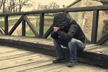 Depressed person with hood sitting on sidewalk.