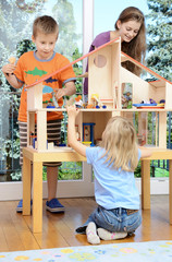 Babysitter und Kinder spielen mit Puppenhaus