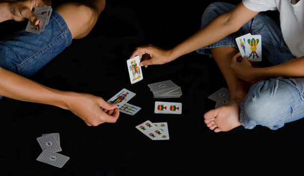 Two boys playing cards on black floor at night