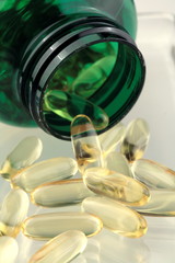 Fish oil capsules falling out of a green bottle