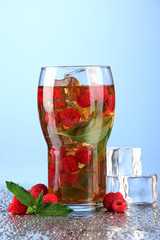 Iced tea with raspberries and mint on blue background