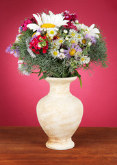 Beautiful bright flowers in vase on table on pink background