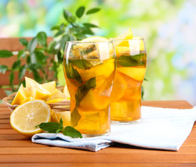 Iced tea with lemon and mint on wooden table, outdoors