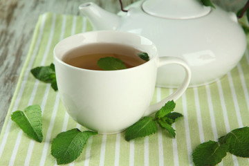 Teapot and cup of herbal tea with fresh mint on wooden table