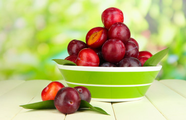 Ripe plums in bowl on wooden table on natural background