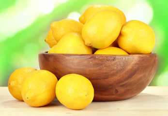 Ripe lemons in bowl on table on bright background