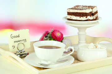 Cup of tea with cakes on wooden tray on table in room