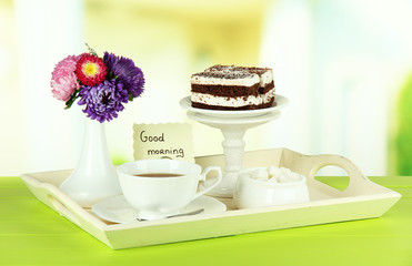 Cup of tea with cakes on wooden tray on table in room