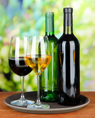 Wine bottles and glasses of wine on tray, on bright background