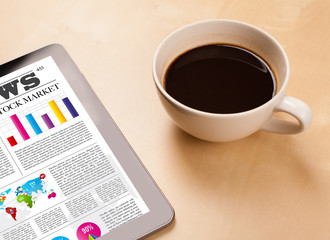 Obraz na płótnie Canvas Tablet pc shows news on screen with a cup of coffee on a desk