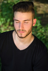 Fototapeta premium Peaceful young man with eyes closed, relaxing outdoors in nature