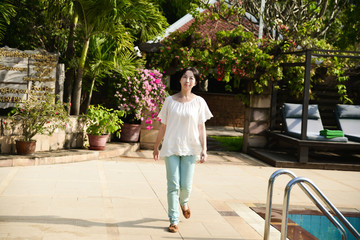 Fototapeta na wymiar Young beautiful woman walking near swimming pool on hotel