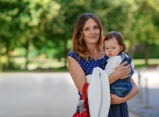 Beautiful mother and little daughter walking in summer park