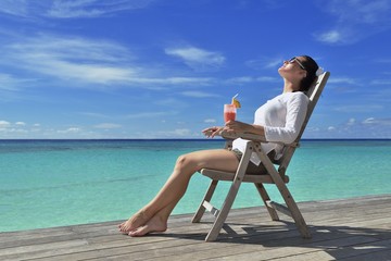 Beautiful young woman with a drink by the sea