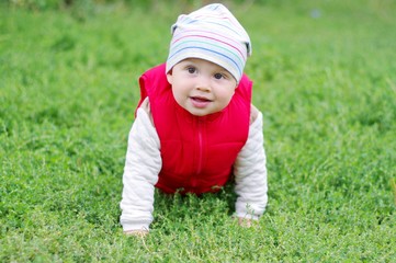 lovely baby in red waistcoat creeps on grass