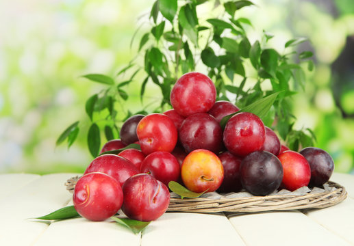 Ripe plums in basket on wooden table on natural background