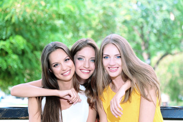 Obraz premium Three beautiful young woman sitting on bench in summer park