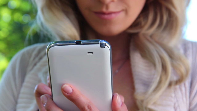 Closeup of smiling blond girl writing message touch phone sms