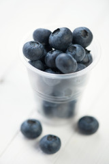 Plastic cup with blueberries on white wooden boards