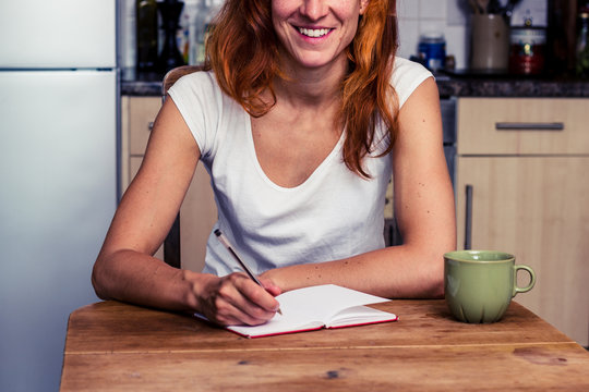 Happy woman writing in her kitchen