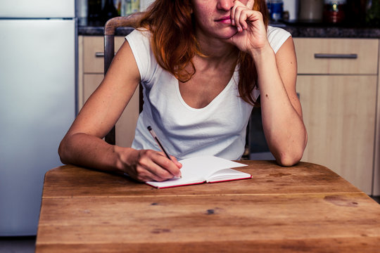 Bored woman writing in her kitchen