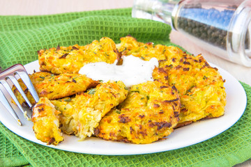 Zucchini pancakes with carrots and sour cream on green towel