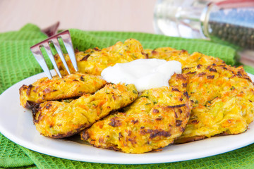 Zucchini pancakes with carrots and sour cream on green towel