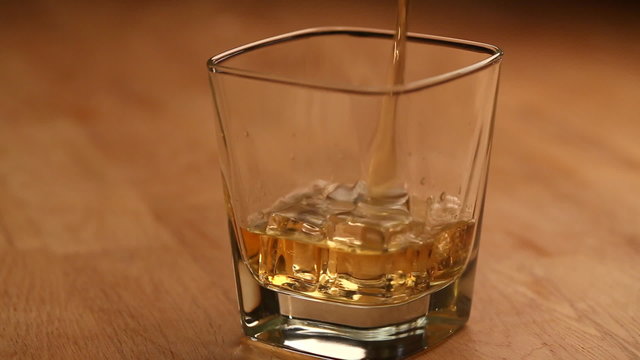 Pouring brandy or whiskey with ice cubes into the glass