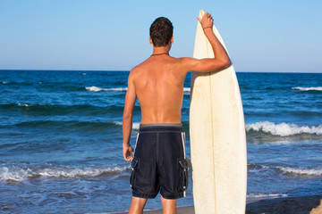 Boy surfer back view holding surfboard on beach