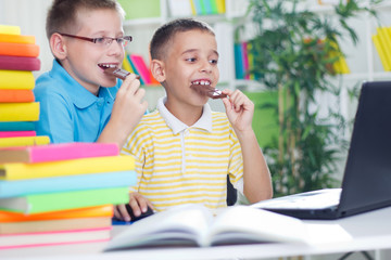 Two young boys eating chocolate and using laptop