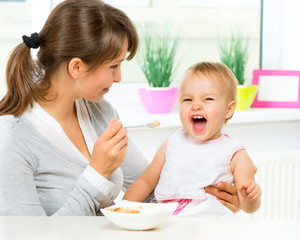 Obraz na płótnie Canvas Mother Feeding Her Baby Girl with a Spoon