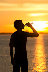 Man drinking bottle of water on the beach at sunrise