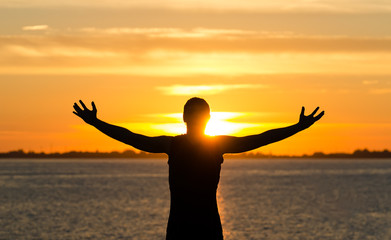Man with arms wide open on the beach at sunrise