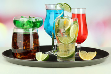 Many glasses of cocktails on tray on table, on bright