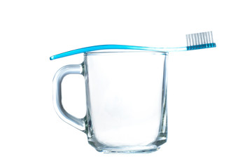 Blue toothbrush rests on a glass mug on white