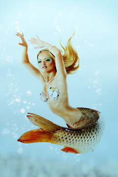 beautiful mermaid girl with fish tail and long blond hair swimmi